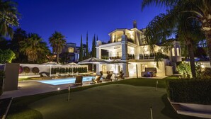 Una casa grande de varios pisos con piscina, mobiliario exterior y palmeras.