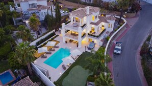 Una casa de varios pisos con piscina, mobiliario de exterior y un jardín cuidado.