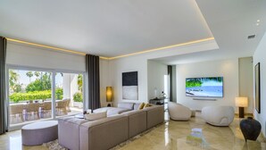 Una sala de estar moderna con un sofá grande, un televisor de pantalla plana y un balcón con mobiliario exterior.