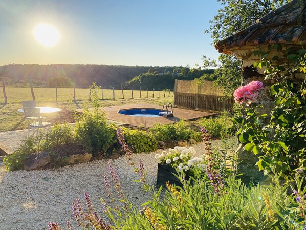 A backyard with a swimming pool, surrounded by a wooden deck, gravel, and various plants and flowers.