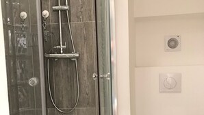 Un baño moderno con ducha envuelta en vidrio, inodoro y calentador de pared.