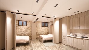 Una habitación pequeña con dos camas, un kitchenette y una pared de piedra.