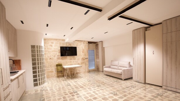 Un interior moderno con suelo estampado de piedra, un televisor de pantalla plana en la pared, un sofá y una zona de comedor con mesa y sillas.