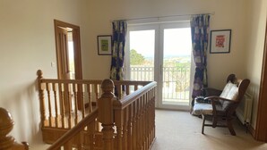 A staircase with wooden balusters leading to a balcony with a view of the countryside. - Stunning modern home in a perfect location (Ballycastle)