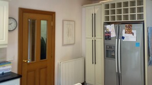 A kitchen with a wooden table, white cabinets, a refrigerator, and a door with a glass panel. - Stunning modern home in a perfect location (Ballycastle)