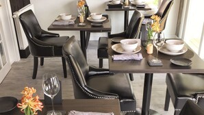 A dining area with black leather chairs, dark wooden tables, and white bowls. - Sea Street Inn (Hyannis)
