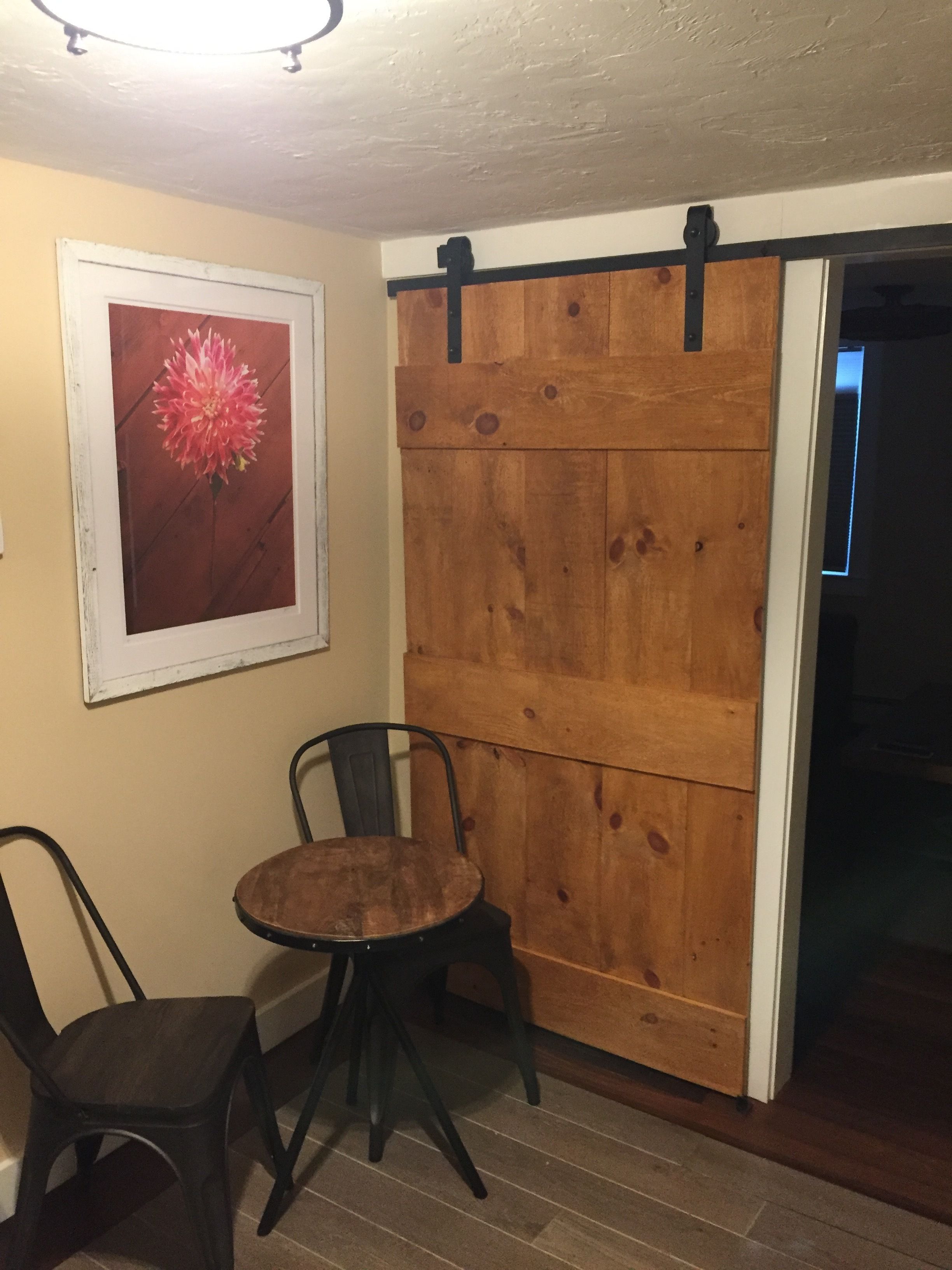 A room with a wooden sliding door, a small round table, two chairs, and a framed picture of a flower on the wall.
