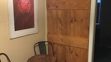 A room with a wooden sliding door, a small round table, two chairs, and a framed picture of a flower on the wall.