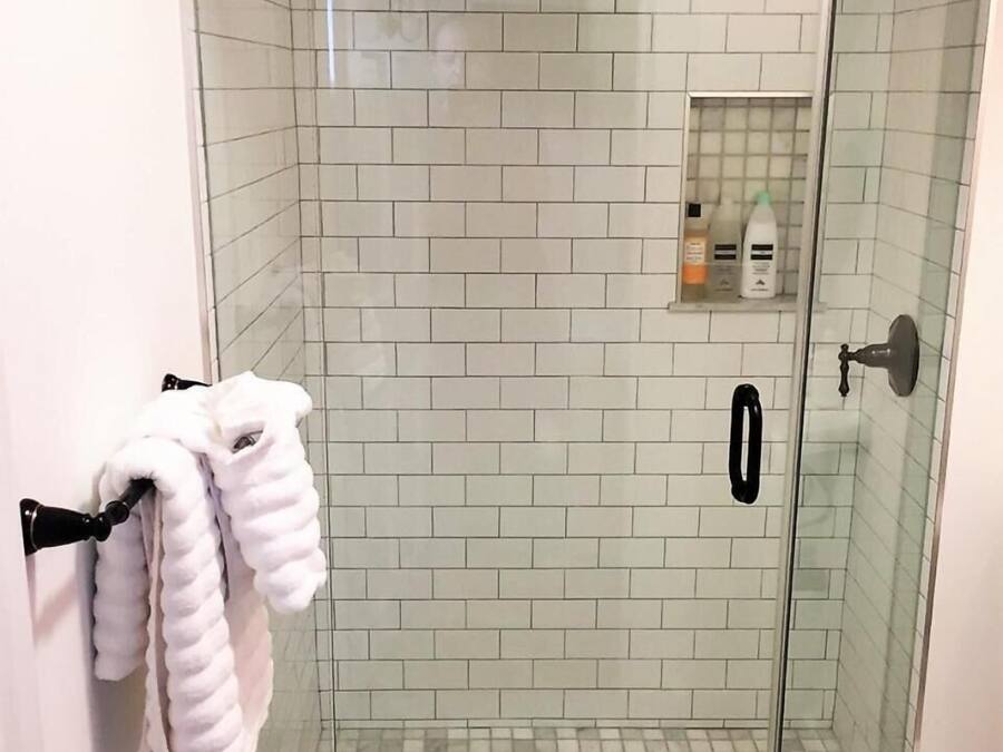 A glass-enclosed shower with white tiles, a towel rack with towels, and a small shelf with toiletries.