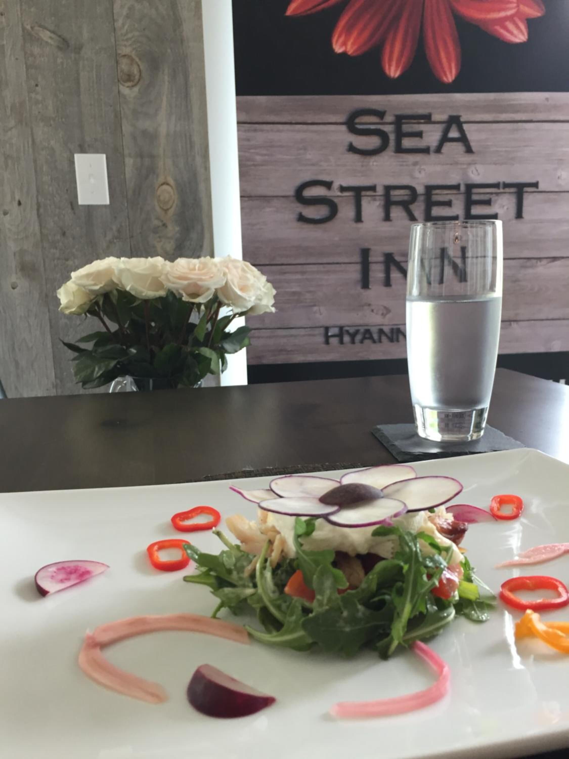 Een eettafel met een bord eten, een glas water en een bloevas.