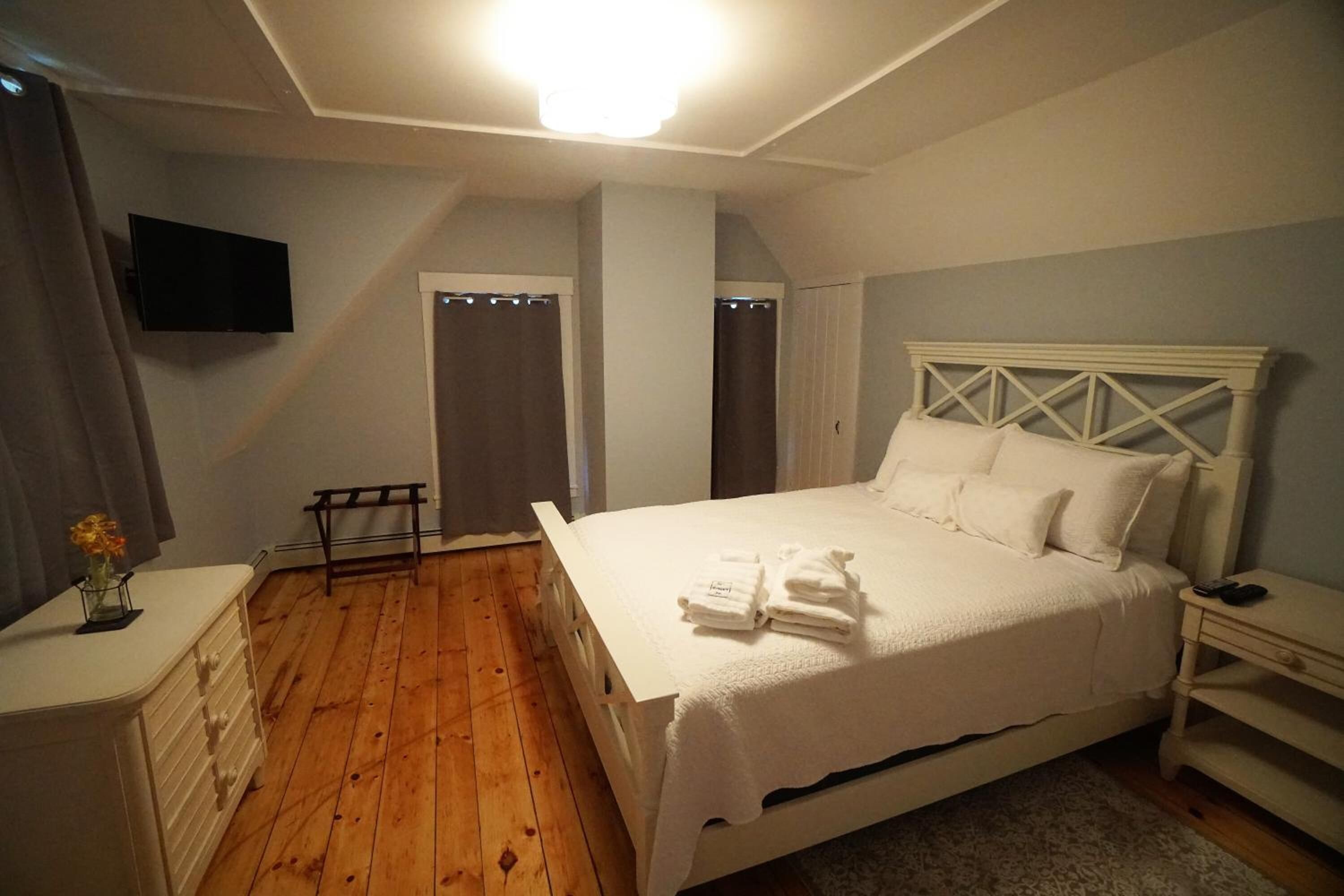 Een slaapkamer met een groot bed, een dressoir, een nachtkastje, een aan de muur bevestigde televisie en een houten vloer.
