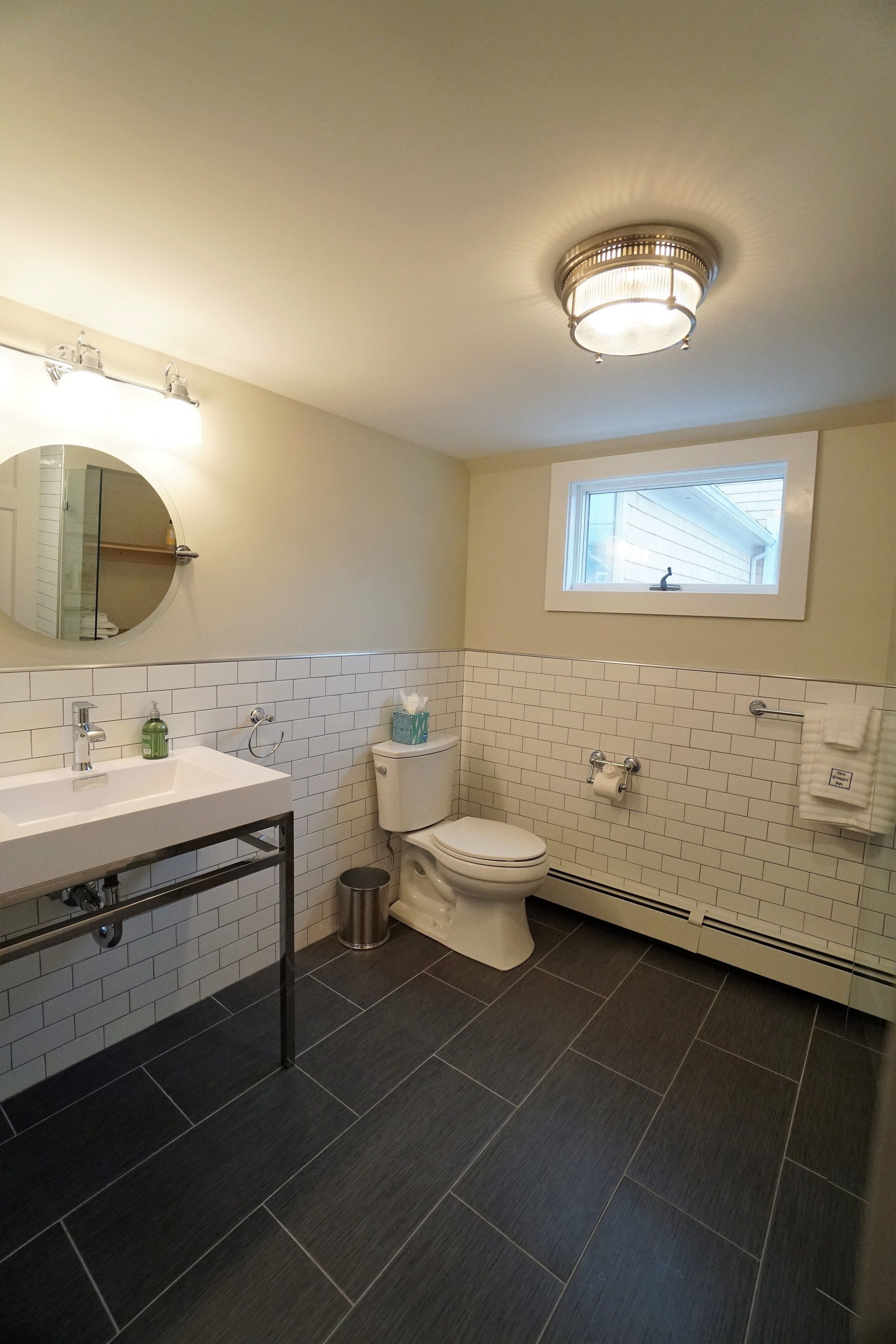 A bathroom with a white sink, a toilet, and a window above the toilet.