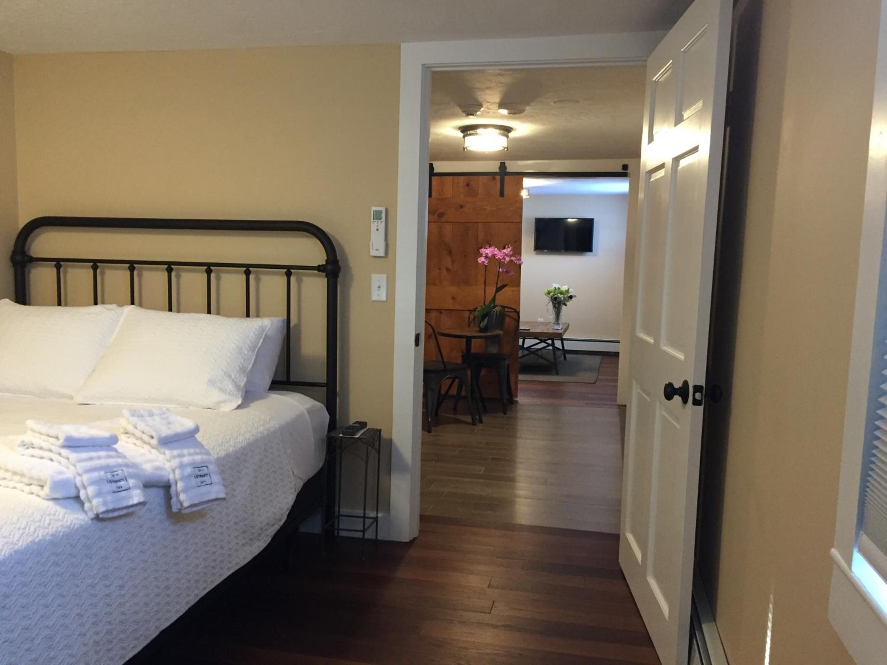 A hotel room with a bed, a small table with chairs, a wooden wall, and a TV mounted on the wall.