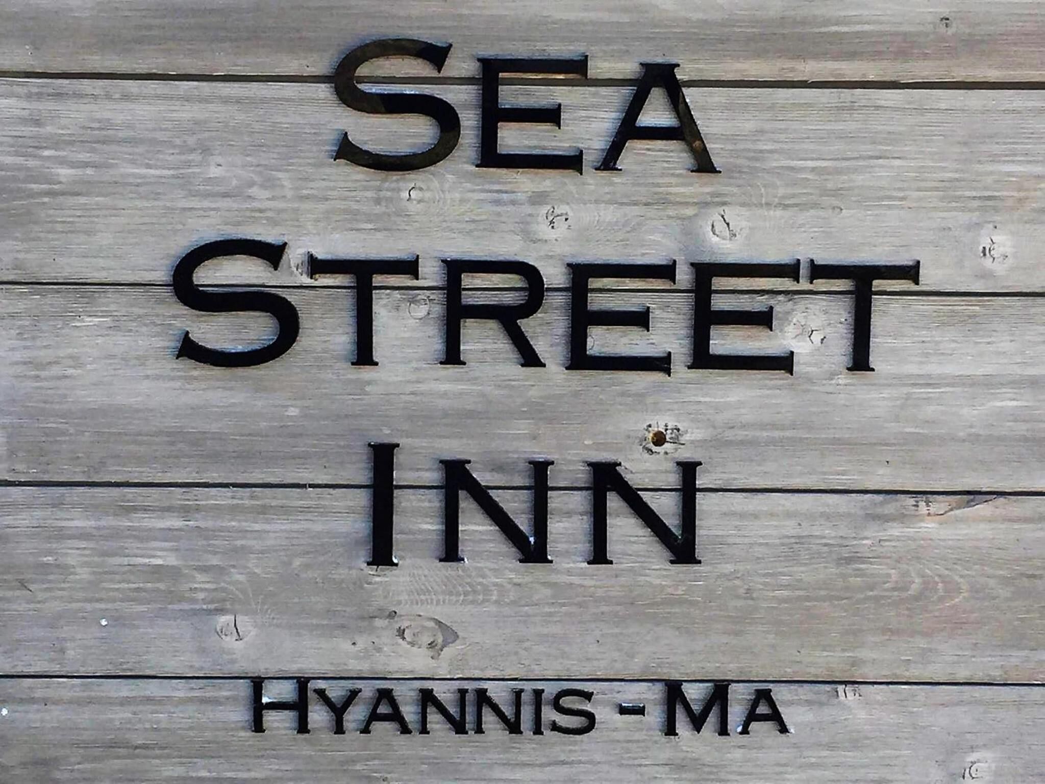 Uma placa de madeira com o texto 'SEA STREET INN' e 'HYANNIS - MA', indicando o nome e a localização da hospedaria.