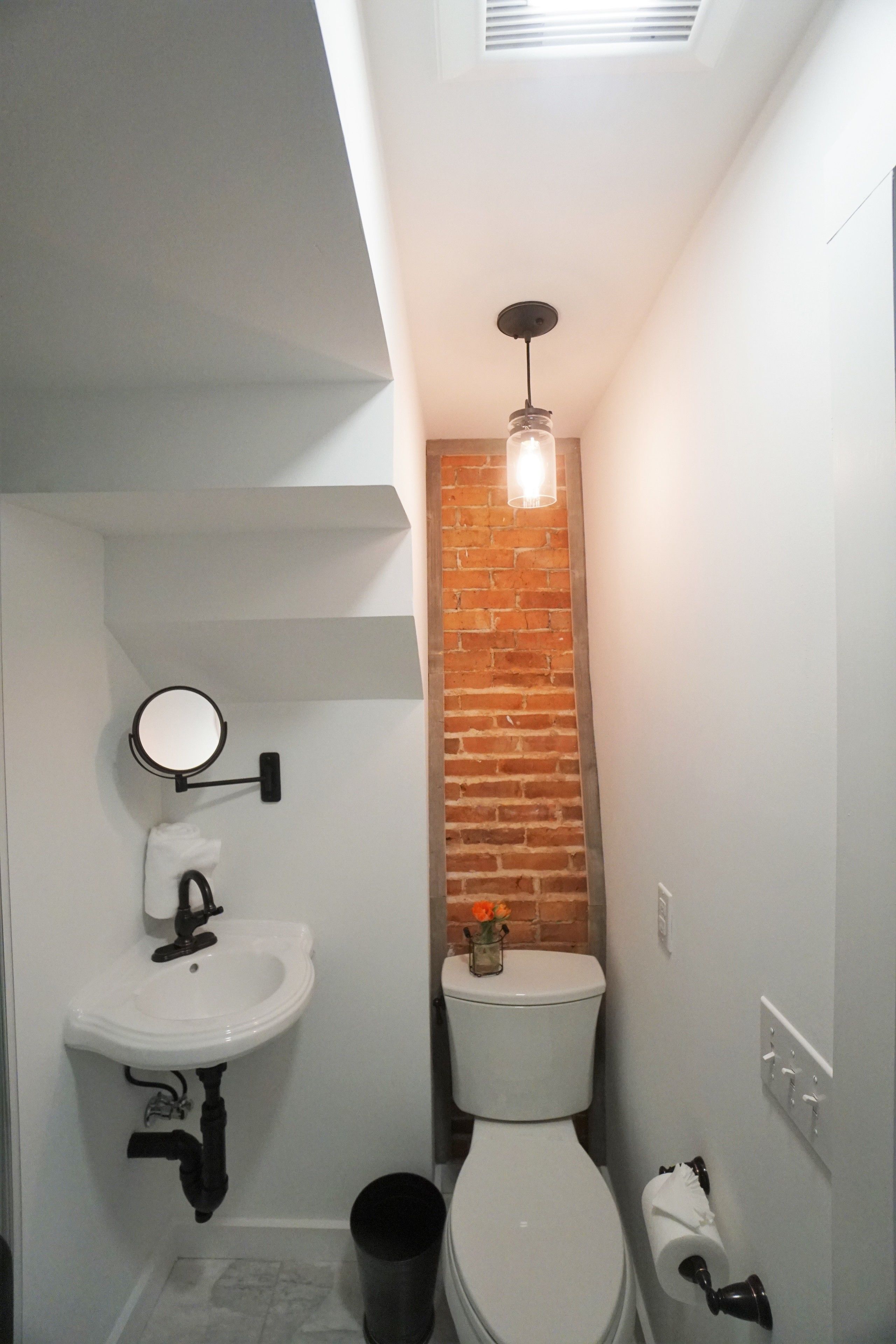 A compact bathroom with a white sink, a round mirror, a toilet, and a small trash bin.