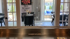 A kitchen counter with a knife and a cutting board, a sign with a flower, and a view of a dining area through glass doors. - Sea Street Inn (Hyannis)