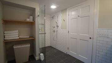 A modern bathroom with a glass-enclosed shower, white tiled walls, and a wooden shelf with towels.