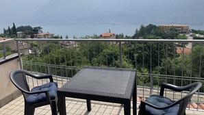 A balcony with a table and two chairs, overlooking a lake and mountains. - La Quiete 56 Holideal Apartment (Tremosine)