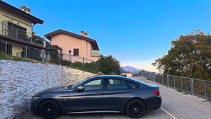 A black car parked in a parking space with a stone wall and a building in the background. - La Quiete 56 Holideal Apartment (Tremosine)