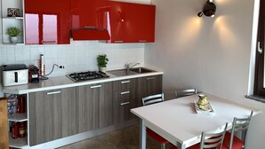 A modern kitchen with red cabinets, a white countertop, and a dining area with a white table and red chairs. - La Quiete 56 Holideal Apartment (Tremosine)