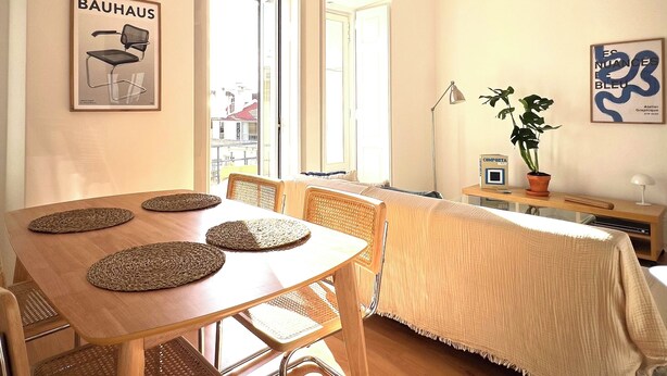 A dining area with a wooden table and chairs, a large window, and artwork on the walls. - Charming Graça - 4 pax (Lisboa)