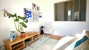 A modern living room with a glass coffee table, a potted plant, a white chair, and artwork on the wall. - Charming Graça - 4 pax (Lisboa)