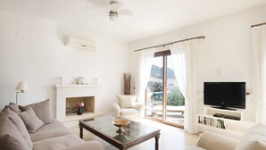 Een woonkamer met een bank, fauteuil, salontafel, open haard, televisie en uitzicht op de omgeving.