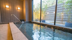 A spa area with a hot tub, wooden walls, and a view of bamboo outside. - Tabino Hotel Sado (Sado)