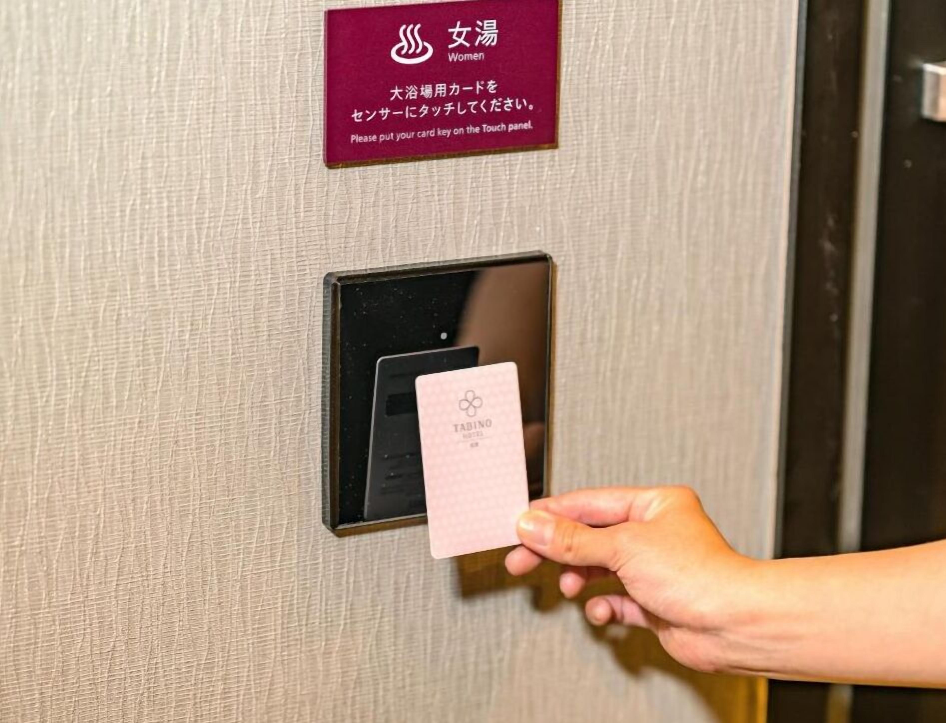A hand holding a card near a touch panel on a door, with a sign above instructing to put the card key on the panel.