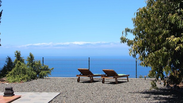 Two wooden lounge chairs facing a clear blue sky and ocean view, with a gravel path and greenery in the foreground. - Casa Luque, La Punta, Spain (Tijarafe)