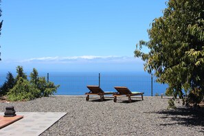 Two wooden lounge chairs facing a clear blue sky and ocean view, with a gravel path and greenery in the foreground. - Casa Luque, La Punta, Spain (Tijarafe)