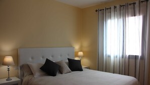 A neatly made bed with a headboard, two bedside lamps, and a window with curtains. - Casa Luque, La Punta, Spain (Tijarafe)