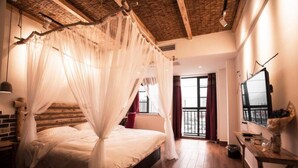 Een slaapkamer met een hemelbed, houten vloeren, een televisie en een balkon met uitzicht.