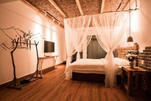 Une chambre à coucher avec un lit sous un baldaquin, un téléviseur posé sur un meuble et un plancher en bois.