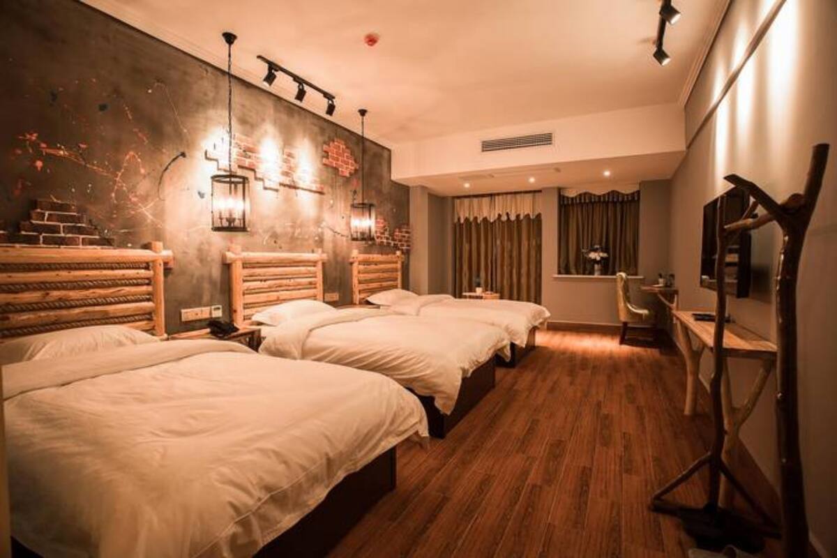 Une chambre d’hôtel avec trois lits, un plancher en bois, un mur en briques et un bureau avec une chaise.
