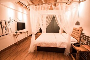 Une chambre à coucher avec un lit sous un dais, une table de chevet, un téléviseur et un mur orné d’une fresque.