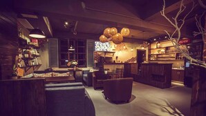 Een gezellige, gedimde bar met houten meubels, hangende bolvormige lampen en een televisiescherm.