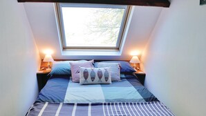 Ein Schlafzimmer mit einem Bett, zwei Nachttischlampen und einem Fenster mit Blick auf Bäume.