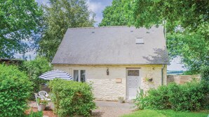 Ein Steinhaus mit geneigtem Dach, einer Haustür und einem kleinen Fenster. Vor dem Haus befindet sich ein Garten mit einer Bank und einem Sonnenschirm.