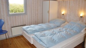Habitación individual con cama, techo de madera, armario, una silla y dos luces fijadas a la pared.
