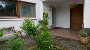 Ett hus med en träbänk, en krukväxt och en hängkorg med blommor.