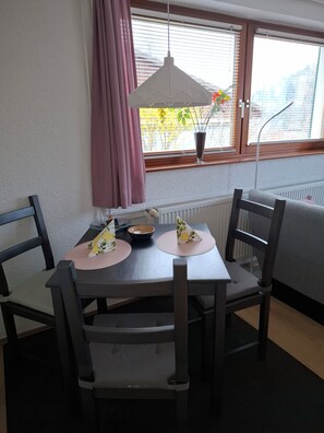 Un comedor con una mesa, sillas, una lámpara colgante, un ventanal con persianas y un radiador.