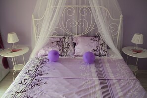A bedroom with a canopy bed, two bedside tables with lamps, and a purple floral bedspread.