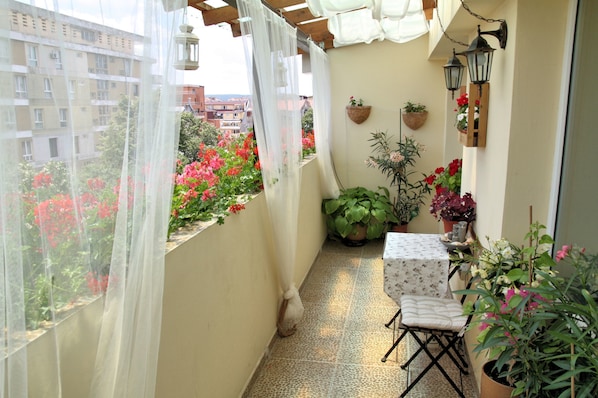 A balcony with a table and chairs, potted plants, and a view of buildings and flowers.
