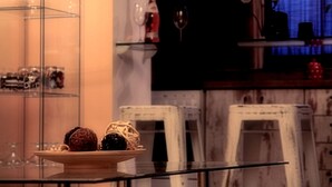 Ein Essbereich mit einem Glastisch, auf dem Geschirr, ein Weinglas und eine Flasche stehen. Im Hintergrund befinden sich Stühle und ein Schrank.