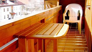 A wooden balcony with a bench, a white plastic chair, and a view of buildings and mountains. - Ferienwohnung II° "Bergstüberl" mit extra Schlafzimmer und Balkon, 60 qm (Aschau im Chiemgau)