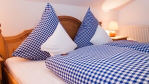 A bed with checkered bedding and pillows, a wooden headboard, a bedside lamp, and a nightstand. - Ferienwohnung II° "Bergstüberl" mit extra Schlafzimmer und Balkon, 60 qm (Aschau im Chiemgau)
