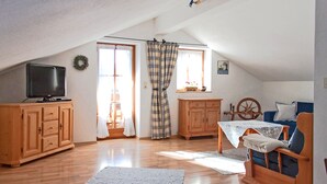 A cozy attic room with wooden floors, a television, a rocking chair, and a window with plaid curtains. - Ferienwohnung II° "Bergstüberl" mit extra Schlafzimmer und Balkon, 60 qm (Aschau im Chiemgau)