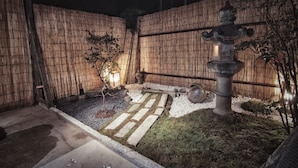 Un jardín japonés tradicional iluminado por la noche, con un farol de piedra, una valla de bambú y un sendero de piedra.