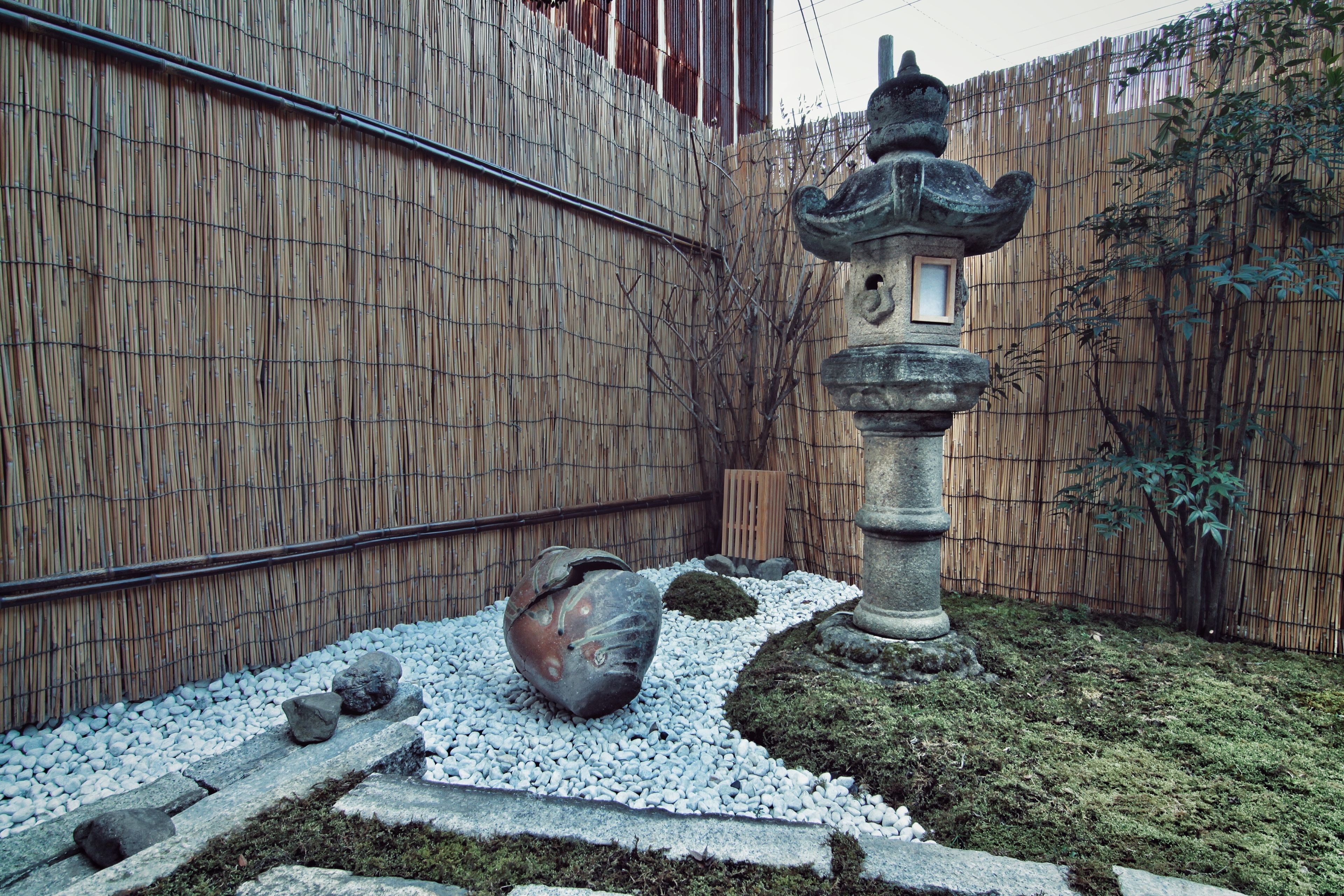A traditional Japanese garden with a stone lantern, moss-covered ground, and a bamboo fence.